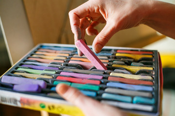 Set of multicolored pastel crayons in open artist box in woman hands. Artist painting on easel