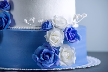 Beautiful two tiered white and blue wedding cake decorated with flowers sugar roses. Concept of elegant holiday desserts