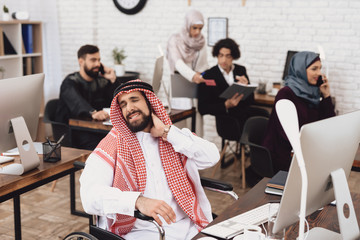 Disabled arab man in wheelchair working in office. Man's neck hurts.