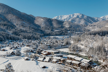 The panoramic viewpoint of Gassho houses in Shirakawago village with snow covered ground ,blue sky and mountains background at winter  in Gifu,Japan.