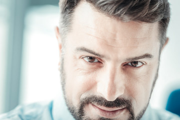 Facial expressions. Handsome brunette wrinkling forehead and keeping smile on face while looking at camera