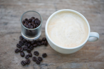 A cup of coffee and bean in glass on wood floor