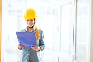 A young happy female engineer with a yellow helmet on her head looking at her blueprint.