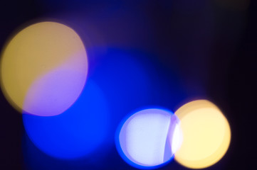 Bokeh light background. Large glowing circles in yellow and blue with a dark background.