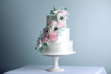 Beautiful three tiered white wedding cake decorated with flowers sugar pink peonies. Concept of elegant holiday desserts