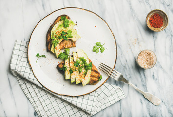 Healthy vegan breakfast or lunch. Flat-lay of avocado toast on plate and seasoning over marble background, top view. Clean eating, detox, weight loss, dieting food concept