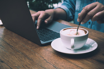 Businessman typing the data into laptop for summary while stirring coffee; business concept by close up