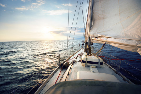 View from a deck of a tilted yacht in strong wind at sunset. Clear sky with glowing golden clouds. Transportation, nautical vessel, cruise, sport, regatta, recreation