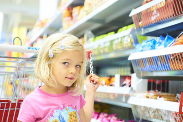 Little Child Blond Girl Shopping in the supermarket, pushing trolley, looking for sweets