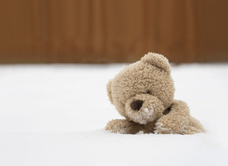 One Teddy bear sitting alone on snow during winter time, A cute brown bear lying on cold snow with blurry wooden wall, Kid soft toy lost in the park