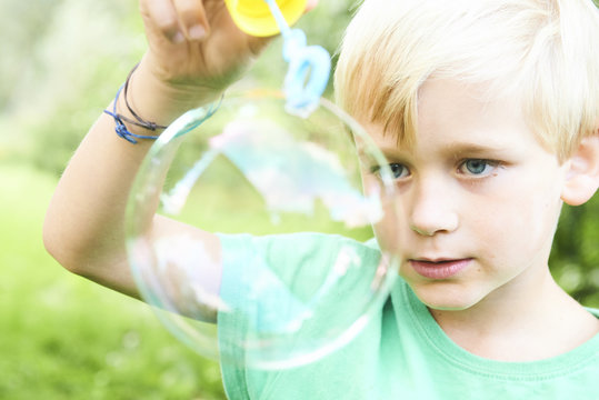 Young boy blowing bubbles with greenery background. Selective focus.

