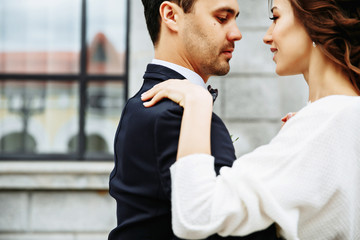 the groom holds his bride in his arms and they dance near the building with beautiful windows