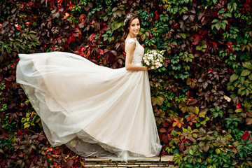 Elegant lady stands in a white lace dress between the walls of green ivy