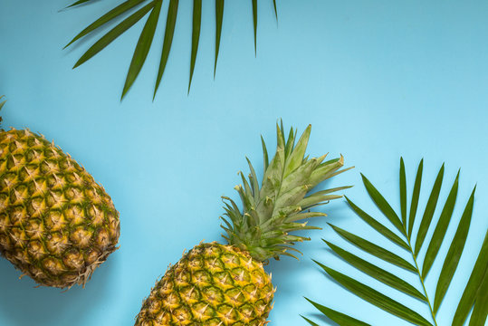 Pineapple and leaves on light blue background, top view, copy space