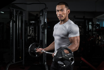 Naklejka premium Muscular builder man training his body with barbell in Modern fitness center