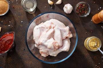 Raw chicken wings and ingredients for bbq sauce on brown rusty background.
