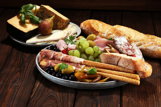 Italian antipasti wine snacks set. Cheese variety, Mediterranean olives, pickles, Prosciutto di Parma, salami and wine in glasses over black grunge background.