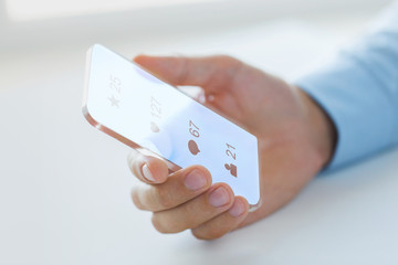 business, future technology and people concept - close up of male hand holding and showing transparent smartphone with social media icons over black background