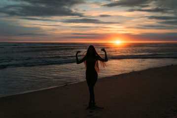 Front view silhouette of attractive woman. Beautiful young girl with long hair walking on the beach, posing at sunset. Concept of travel, relax, yoga