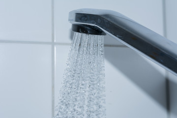 Spritzendes Wasser aus dem Duschkopf im Badezimmer auf weiß