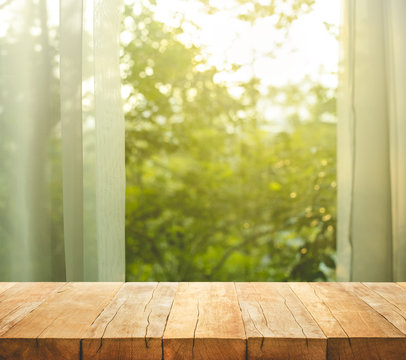 Fototapeta Empty of wood table top on blur of curtain with window view green from tree garden background