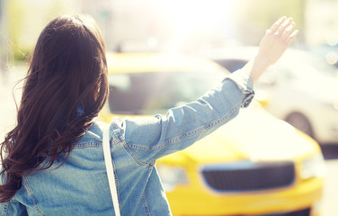 gesture, transportation, travel, tourism and people concept - young woman or teenage girl catching taxi on city street or hitch-hiking