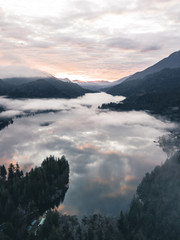 Aerial Photography of cloud ocean above mountain lake surrounded by pinetrees wirh morning glow near Washington, USA