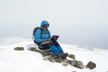 traveler working with a laptop in winter on top of a mountain during the snowfall