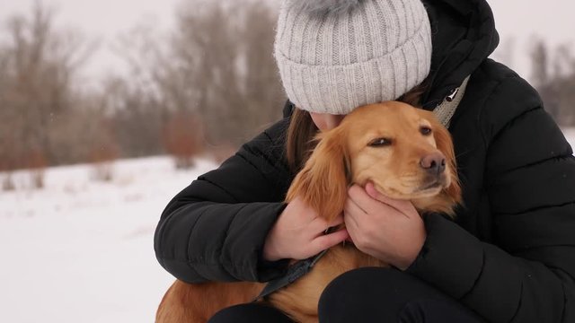Woman scratches dog behind her ear and smiles. Happy owner walks with his dog over snow park.