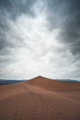 Huge sand dune with moody clouds above in the desert by Death Valley National Park, California USA