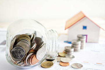 Glass cup collect coin on paper document and blur stack of money house model on background