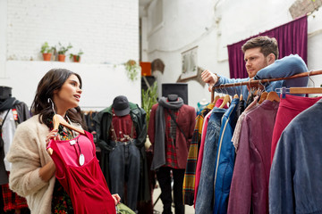 sale, shopping, fashion and people concept - couple choosing clothes at vintage clothing store and...