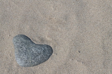 Heart shaped pebble stone half covered with sand laying in the sun