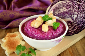 Cream soup made of red cabbage with croutons and parsley on wooden table