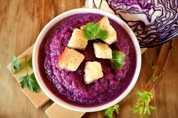 Cream soup made of red cabbage with croutons and parsley on wooden table