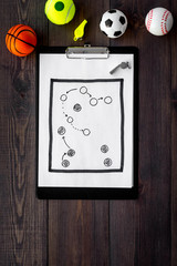 Sport coach concept. Pad with tactic plan of the match near whistle and balls on wooden background...