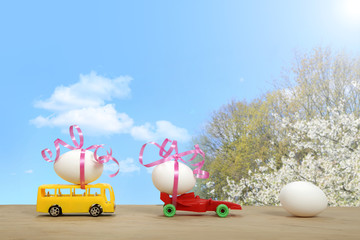 Jaja Wielkanocne na samochodach na tle błękitnego nieba i kwitnących wiśni w promieniach słońca. - obrazy, fototapety, plakaty