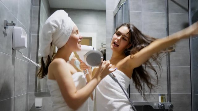 hen-party, attractive Girlfriends into bath towels dance and sing in dryer as in microphone at shower