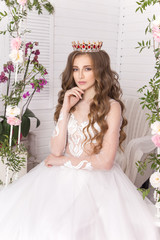 Young girl in the crown and white dress in the studio on a light background