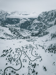 Aerial Photograph of Italian Mountain pass showing a black road winding up the snow covered maountain through pinetrees, Italy 