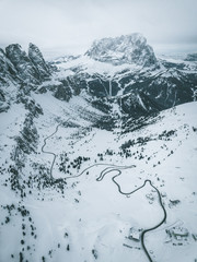 Aerial Photograph of Italian Mountain pass showing a black road winding up the snow covered maountain through pinetrees, Italy 