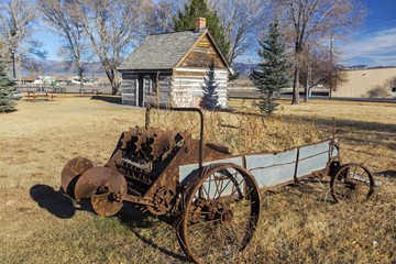 Obraz premium Rusted Wagon Wheel in front of old Wild West Log Cabin in Mormon Pioneer Heritage Park, Scenic Highway 89 near City of Panguitch, Utah