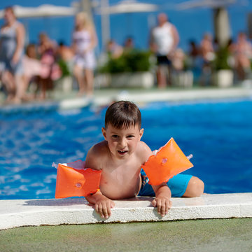 Cute Caucasian boy getting out from the swimming pool through its side.