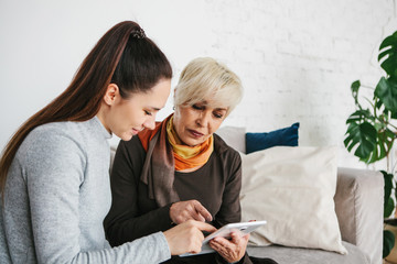 A young girl explains to an elderly woman how to use a tablet or shows some application or teaches you how to use a social network. Teaching the older generation of new technologies.