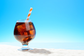Refreshing Cola with ice in glass on the sandy coast