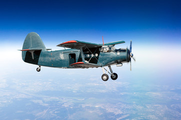 Small aircraft turboprop biplane at high altitude in the sky above the ground with an open door.