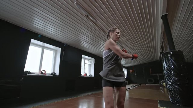 Young girl in sports clothes working out at the gym and using jump rope to perform jumping exercise with side swings