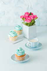 Blue pastel vertical banner with decorated cupcakes, cup of coffe with milk and bouquet of pink roses.