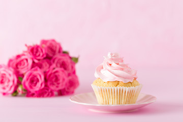 Cupcake with pink cream decoration and roses on pink pastel background.