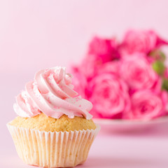 Cupcake with pink cream decoration and roses on pink pastel background.